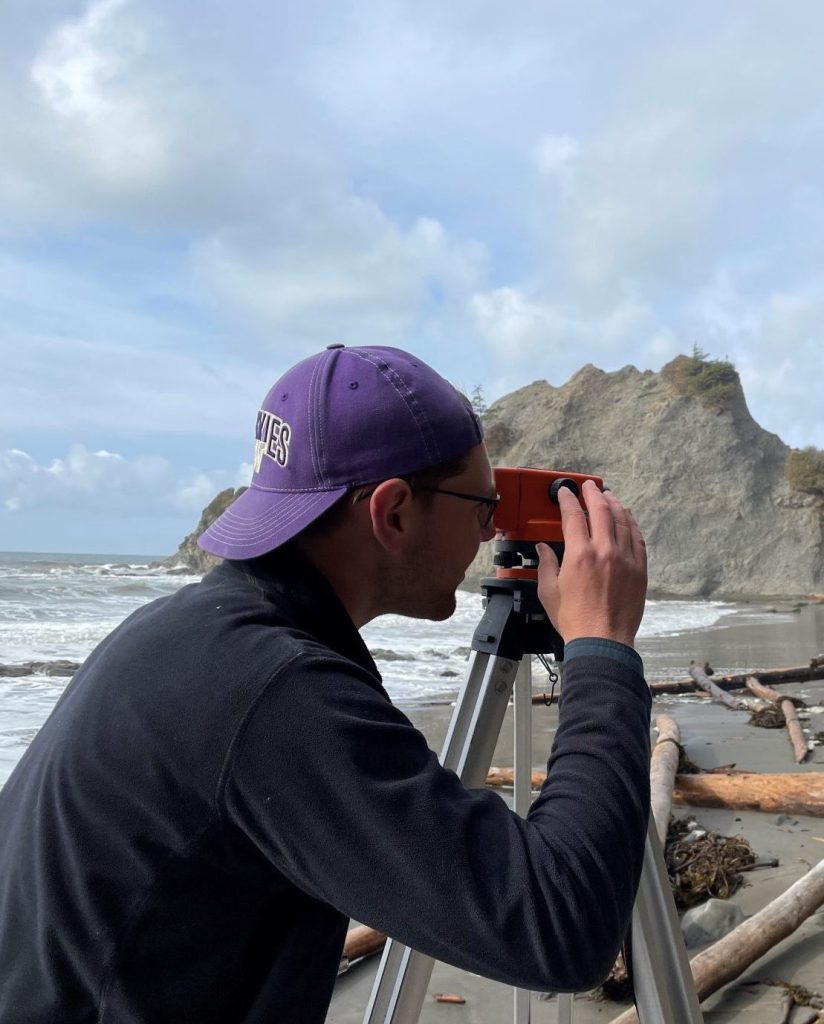 Marquis Richardson in purple Huskies hat using field equipment on a beach.