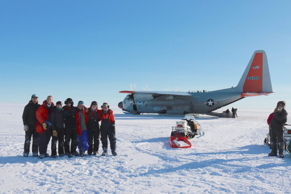 Researchers pose on snow in front of a plane during field work in Antarctica.