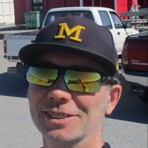 Closeup of Mike Town smiling at the camera wearing sunglasses and a baseball cap.