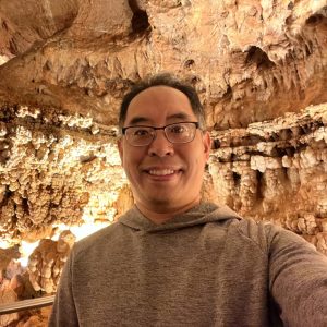 Close up of Henry Lui with a lit up cave wall behind him.
