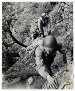 Black and white image of soldiers climbing a rock, photo taken looking down at climbers.