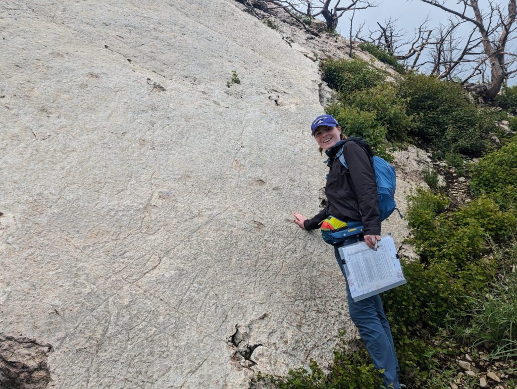 Annika Jorgenson leaning against a large rock face holding a clipboard.