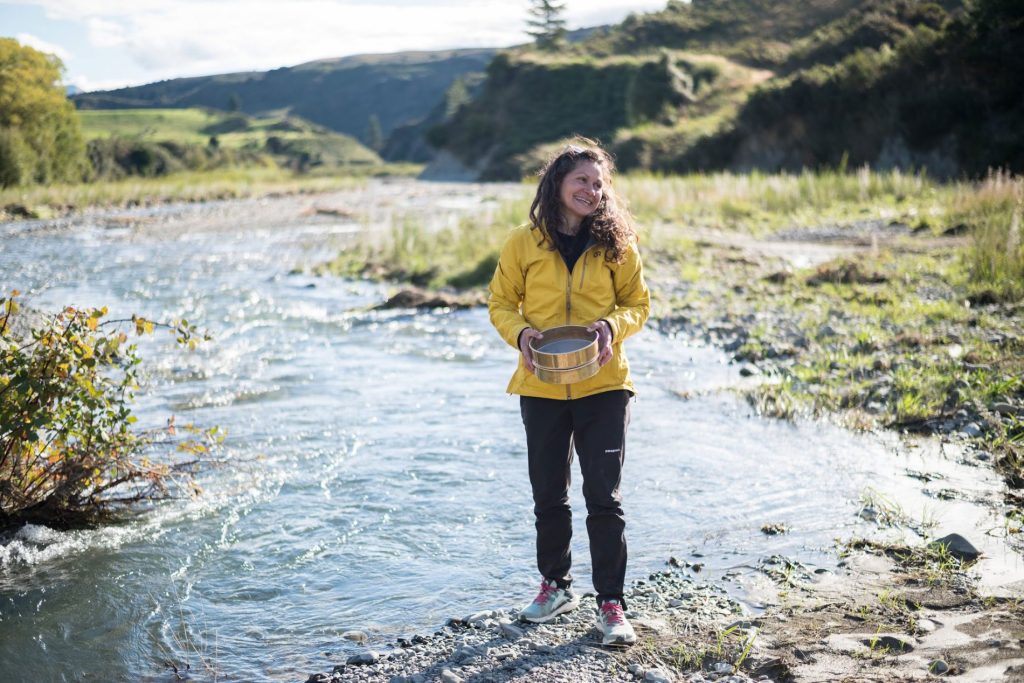 Alison Duvall holds a rock standing in a river.