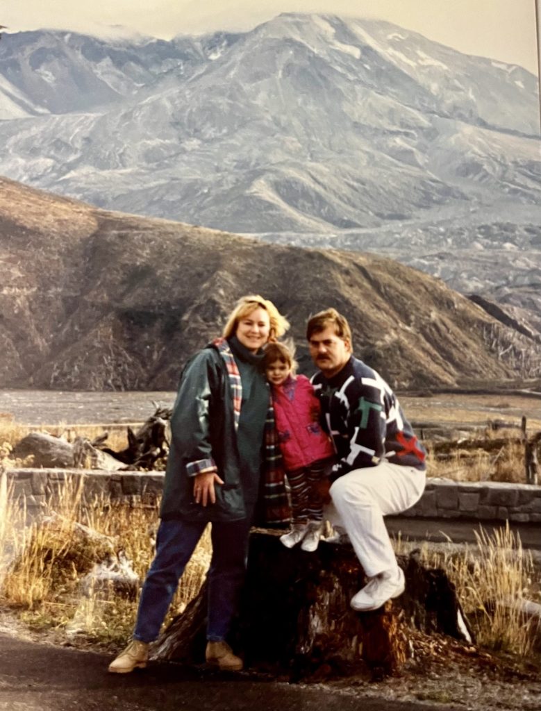 Katie Lambert as a child standing between two adults with mountains in the background.