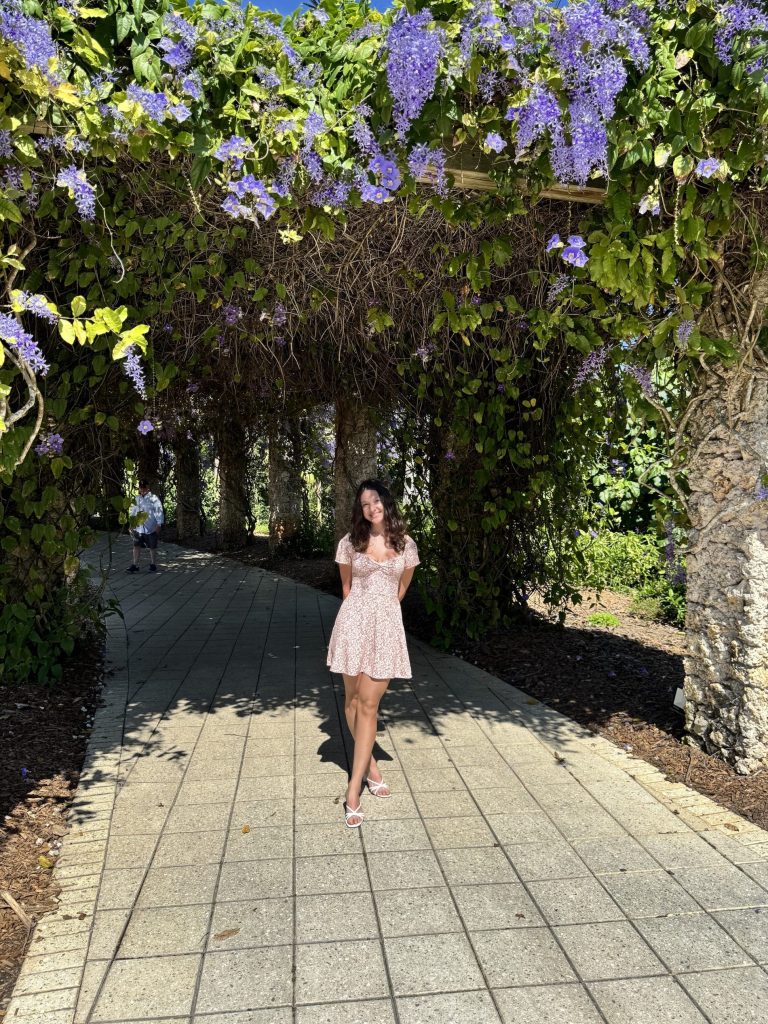 Rosie Ramos standing on a pathway under an arch with flowers.