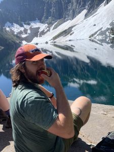 Close up of Jonathan Gates eating an apple with a lake and mountain behind him.