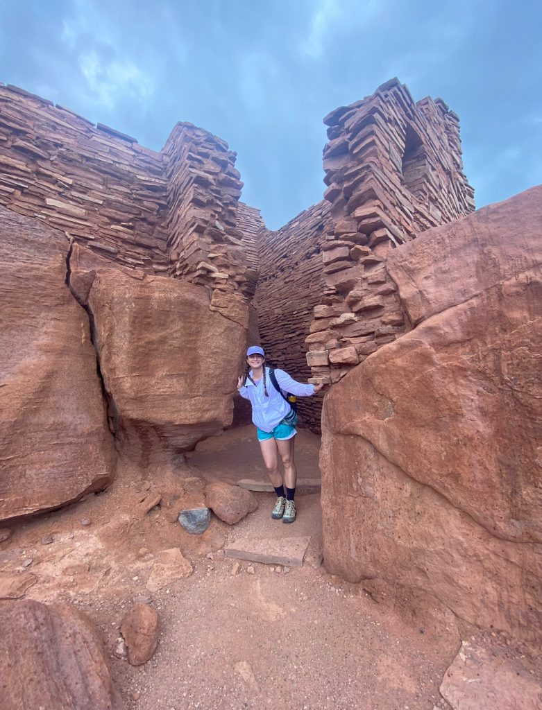 Katie Lambert standing on a red rock with layered red sandstone in the background.