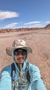 Close up of Vigash Ravi with red sand and mountains behind him.