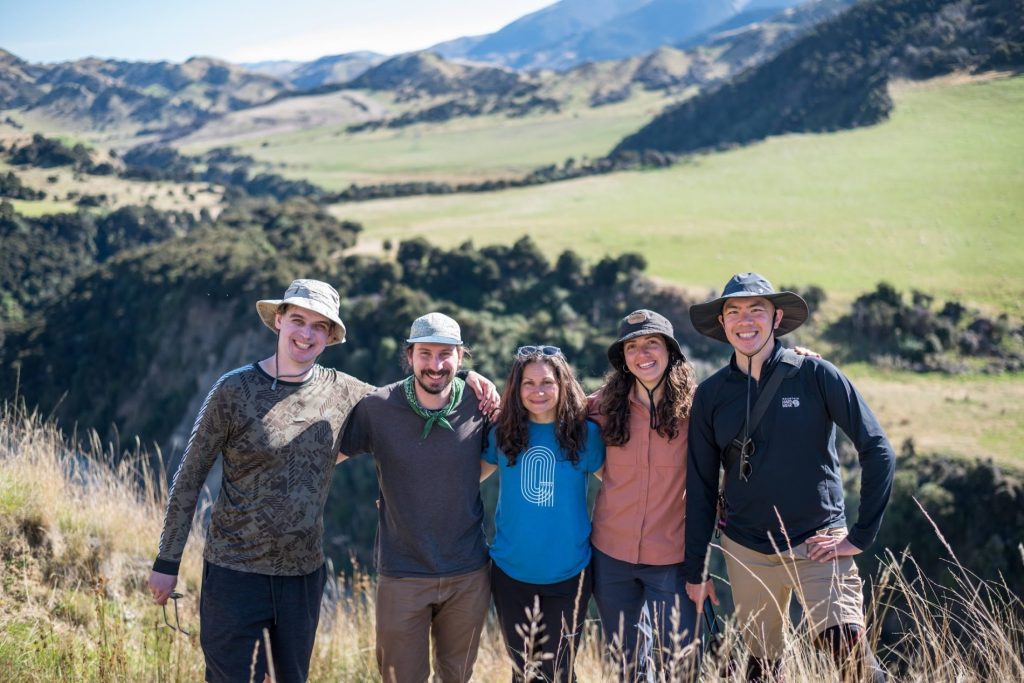 A group of five pose for a photo with grassy hills behind.