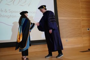 A faculty advisor presenting a graduating graduate student with a hood,