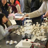 A young kid builds a structure with marshmallows and sticks. The structure sits on a plate that moves, simulating an earthquake.