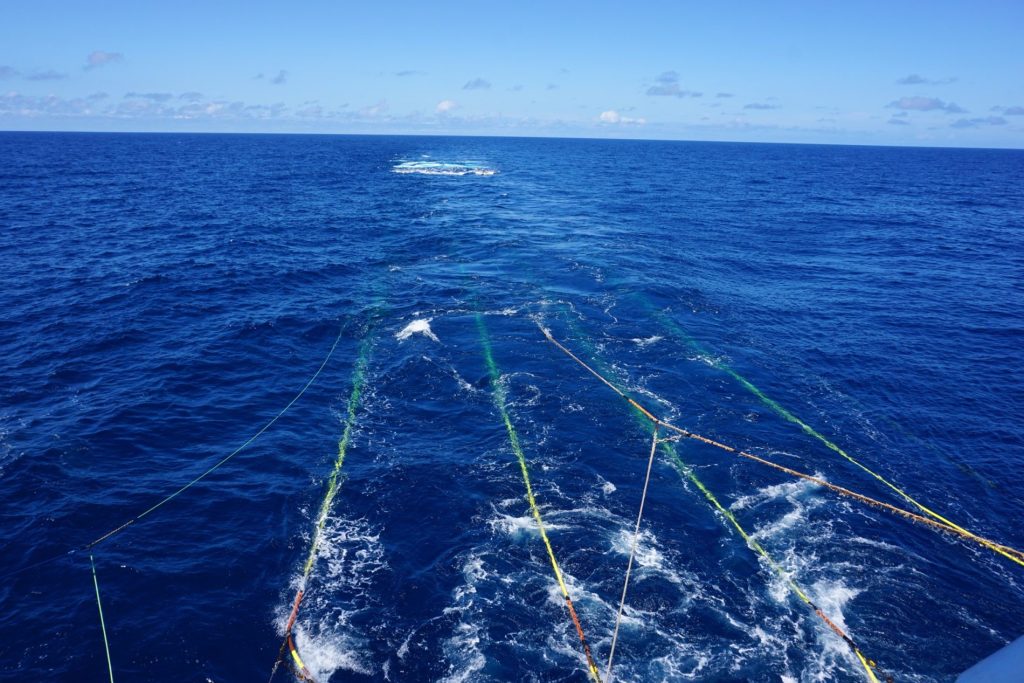 Four lines in ocean towing equipment through the water behind a research vessel.