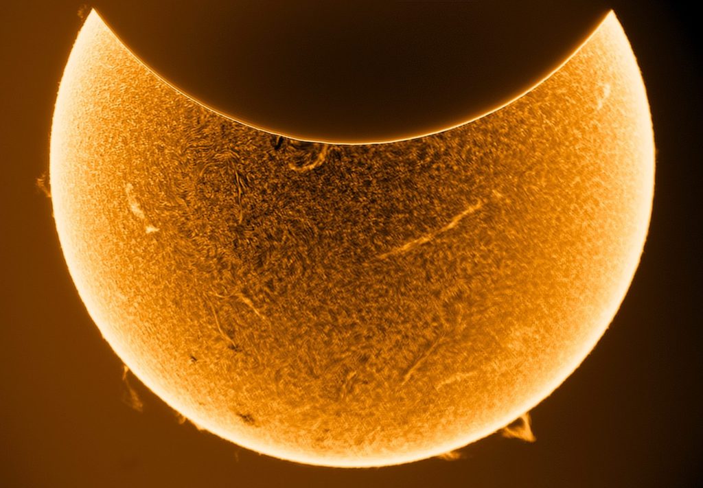 Orange sun starting to be eclipsed by the moon on a black background.