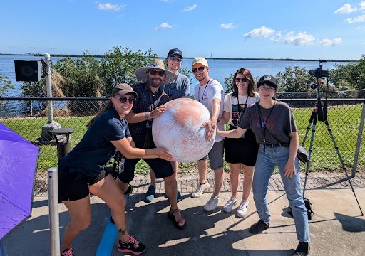 Five people standing around and holding a globe of Europa while smiling at the camera in the sun.