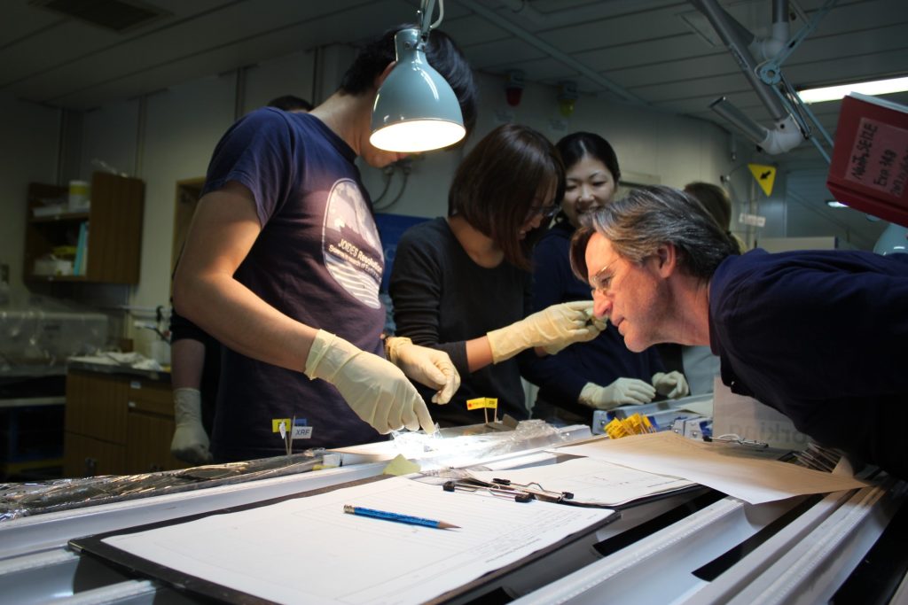 Harold Tobin with colleagues, leaning over a table looking at a sedimentary core.