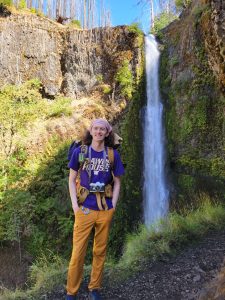 Garrett Stromberg standing in front of a tall waterfall.