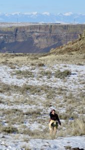 Maro Savvides walking on a snowy, grassy desert with a rock cliff in the far distance.