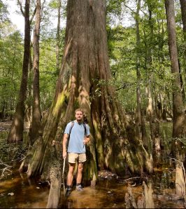 Aidan Dealy standing in shallow water in front of a large tree.