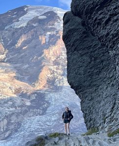 Lauren Woods standing next to a rock wall with a glaciated mountain in the background.