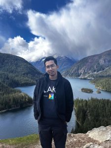 Hamzi Rapi standing with mountains and a lake in the background.