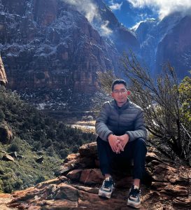 Hamzi Rapi sitting on a rock with a mountain valley in the background.