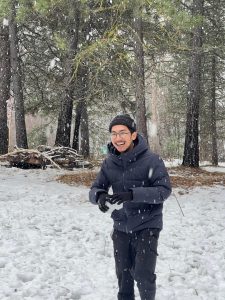 Hamzi Rapi making a snowball laughing with a snowy ground and trees in the background.