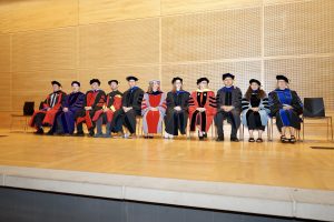 Faculty sitting on stage in their regalia.