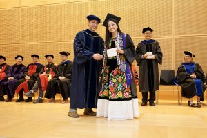 Professor and Chair David Schmidt and undergraduate in cap and gown shaking hands on stage.