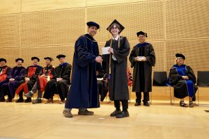 Professor and Chair David Schmidt and undergraduate in cap and gown shaking hands on stage.