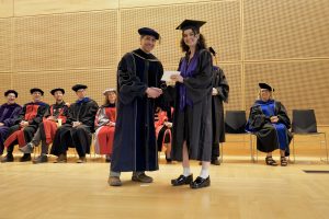 Professor and Chair David Schmidt and undergraduate in cap and gown shaking hands on stage.