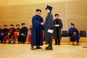 Professor and Chair David Schmidt and undergraduate in cap and gown shaking hands on stage.