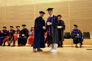 Professor and Chair David Schmidt and undergraduate in cap and gown shaking hands on stage.