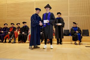 Professor and Chair David Schmidt and undergraduate in cap and gown shaking hands on stage.