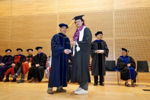 Professor and Chair David Schmidt and undergraduate in cap and gown shaking hands on stage.