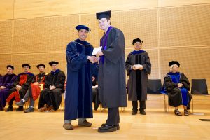Professor and Chair David Schmidt and undergraduate in cap and gown shaking hands on stage.