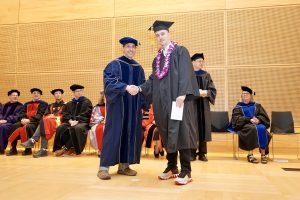 Professor and Chair David Schmidt and undergraduate in cap and gown shaking hands on stage.