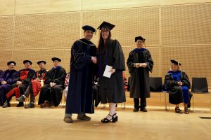 Professor and Chair David Schmidt and undergraduate in cap and gown shaking hands on stage.