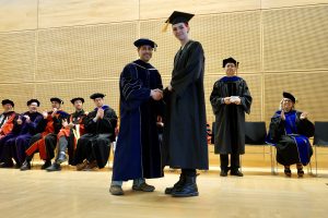 Professor and Chair David Schmidt and undergraduate in cap and gown shaking hands on stage.