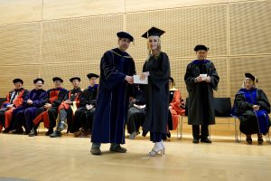 Professor and Chair David Schmidt and undergraduate in cap and gown shaking hands on stage.