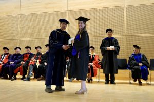 Professor and Chair David Schmidt and undergraduate in cap and gown shaking hands on stage.