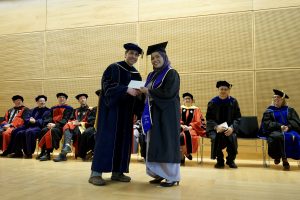 Professor and Chair David Schmidt and undergraduate in cap and gown shaking hands on stage.