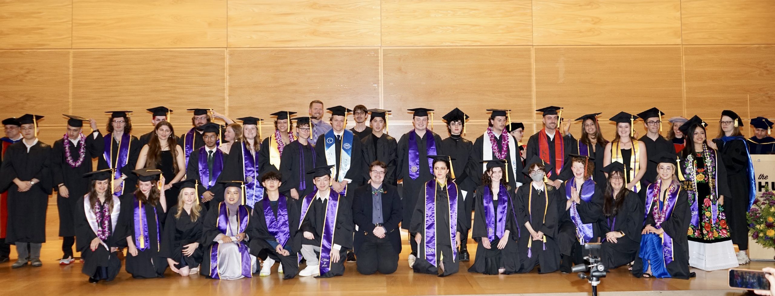 Class of 2025 undergraduates standing on stage in caps and gowns with ESS faculty.