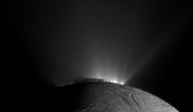 A black and white photo showing the moon Enceladus. Bright jets of water erupt from the subsurface.