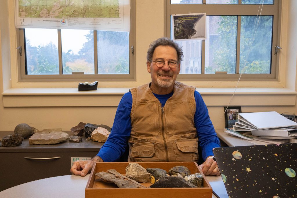 Terry Swanson sitting at his desk with a tray of different rocks in front of him.
