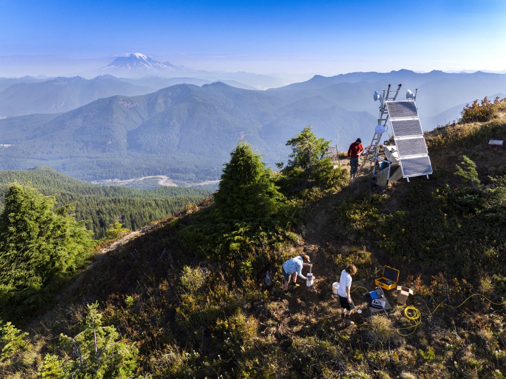 Researchers install seismic monitoring equipment on Burley Mountain with Mt. Rainier visible in the background.