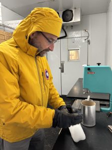 Eric Steig in a yellow parka holding an ice core from 1776 in a cold lab.