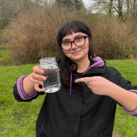 Deven Loska holding up a glass jar with a clear liquid in it.