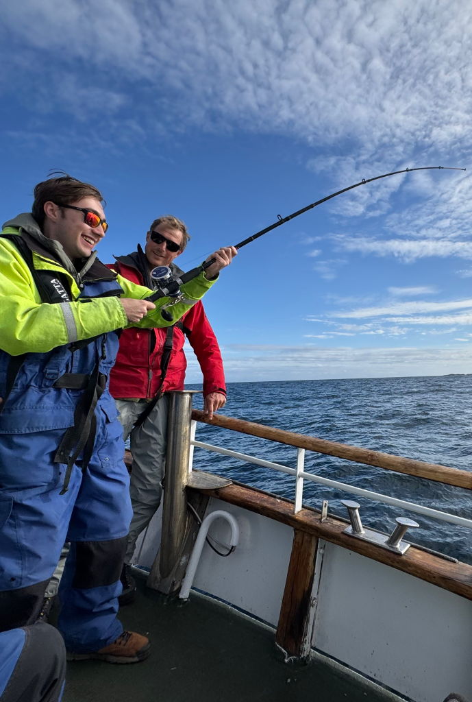 Nate Nolan holding a fishing rod in protective gear on a boat.