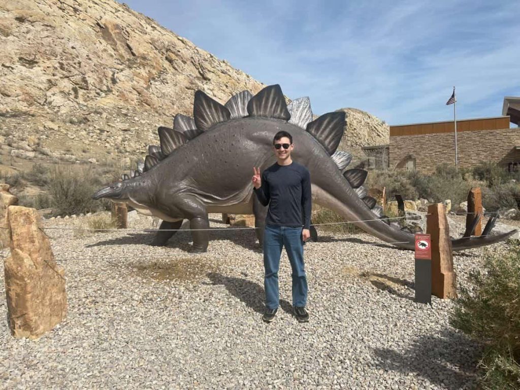 Emmanuel Larsen standing in front of a replica model of a dinosaur.