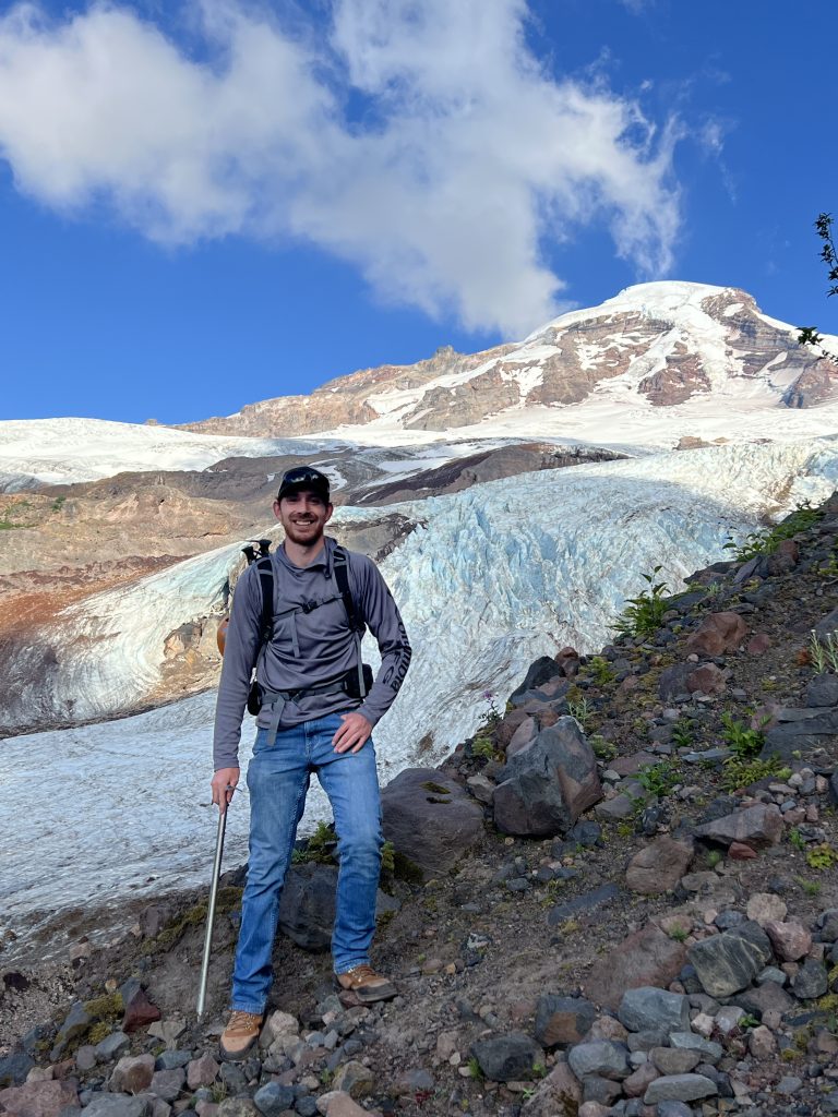 Charles Fleming standing on a ridge with a glacier and mountain in the background.